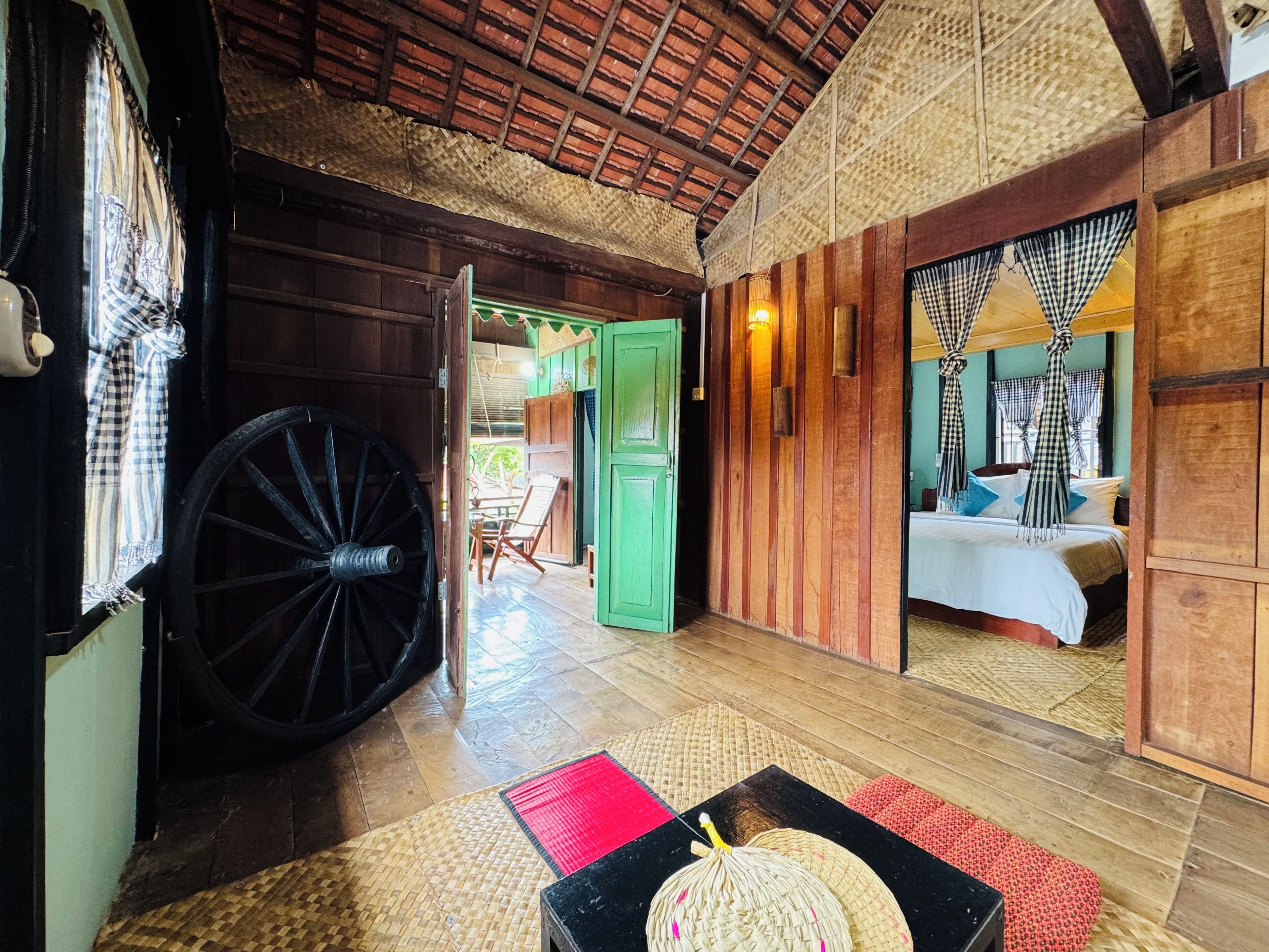 Una habitación de madera tradicional con un gran carrusel, una cama con cortinas de cuadros y una puerta verde que da a otra habitación.