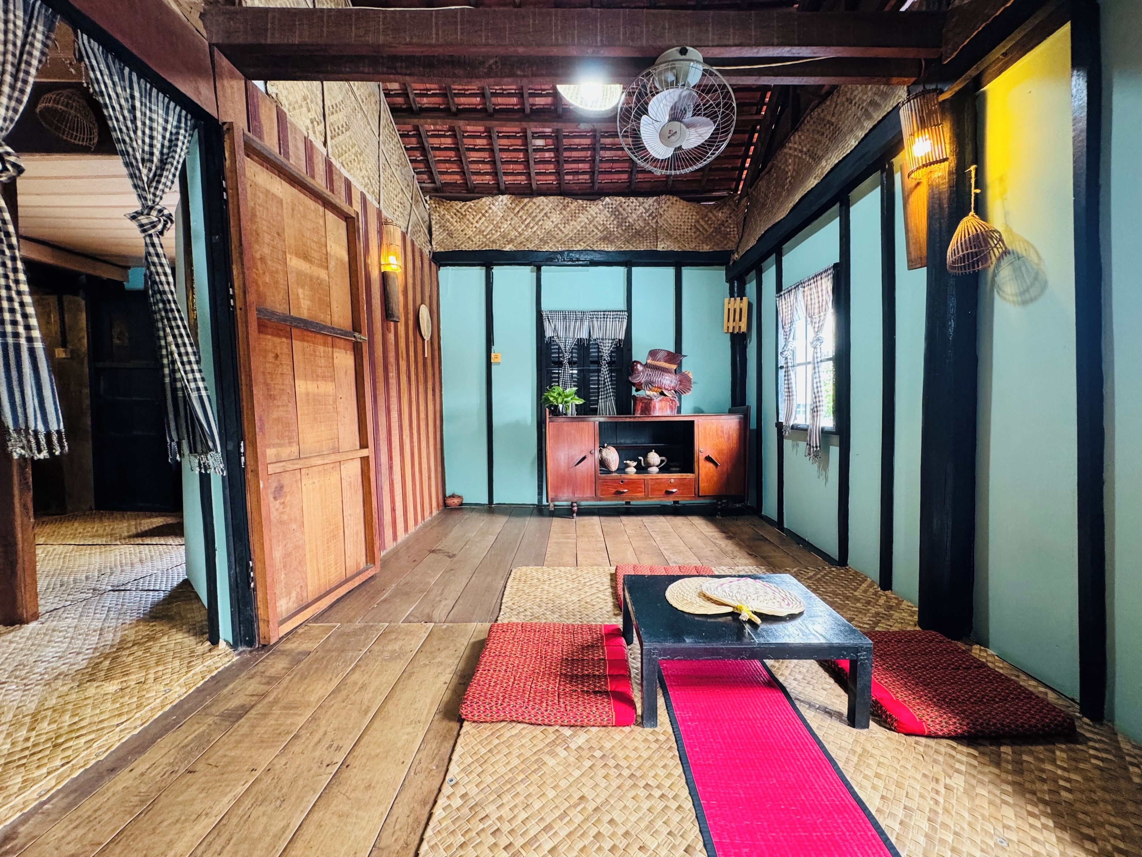 A traditional room with a wooden floor, a black table with a red mat, a fan, and a wooden cabinet with decorative items.