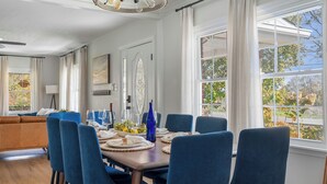 Comedor con mesa de madera dispuesta para seis personas, sillas azules y vista a los árboles a través de amplios ventanales.