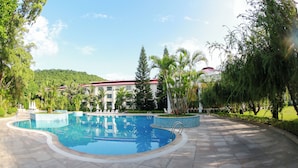 A swimming pool with a tiled deck, surrounded by palm trees and a building with a red roof in the background. - Doson Resort (Hai Phong)