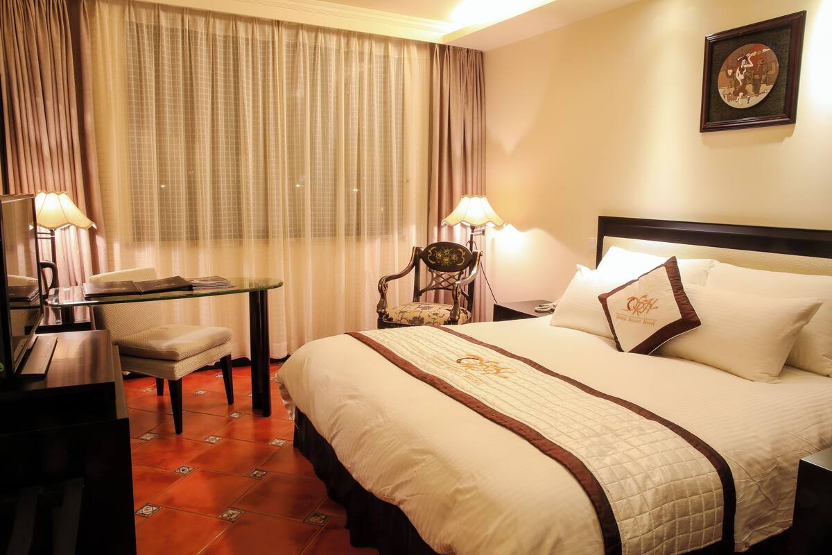 A hotel room with a large bed, a desk with a chair, a lamp, and a framed picture on the wall.