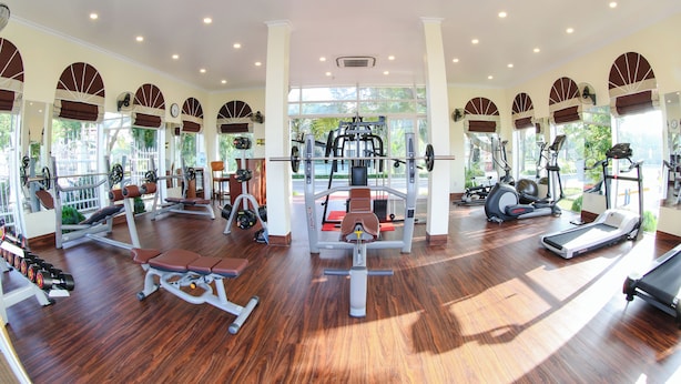 A spacious gym with various exercise equipment, large windows, and a wooden floor. - Doson Resort (Hai Phong)