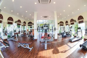 A spacious gym with various exercise equipment, large windows, and a wooden floor. - Doson Resort (Hai Phong)