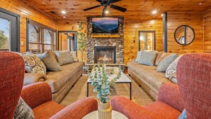 A cozy cabin interior with two sofas, a coffee table, a fireplace, and a ceiling fan. - Sleeps 32: Perfectly Designed For Groups/Reunions! (Gatlinburg)