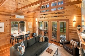 A wooden cabin interior with a dining area, sofa, and a fireplace.