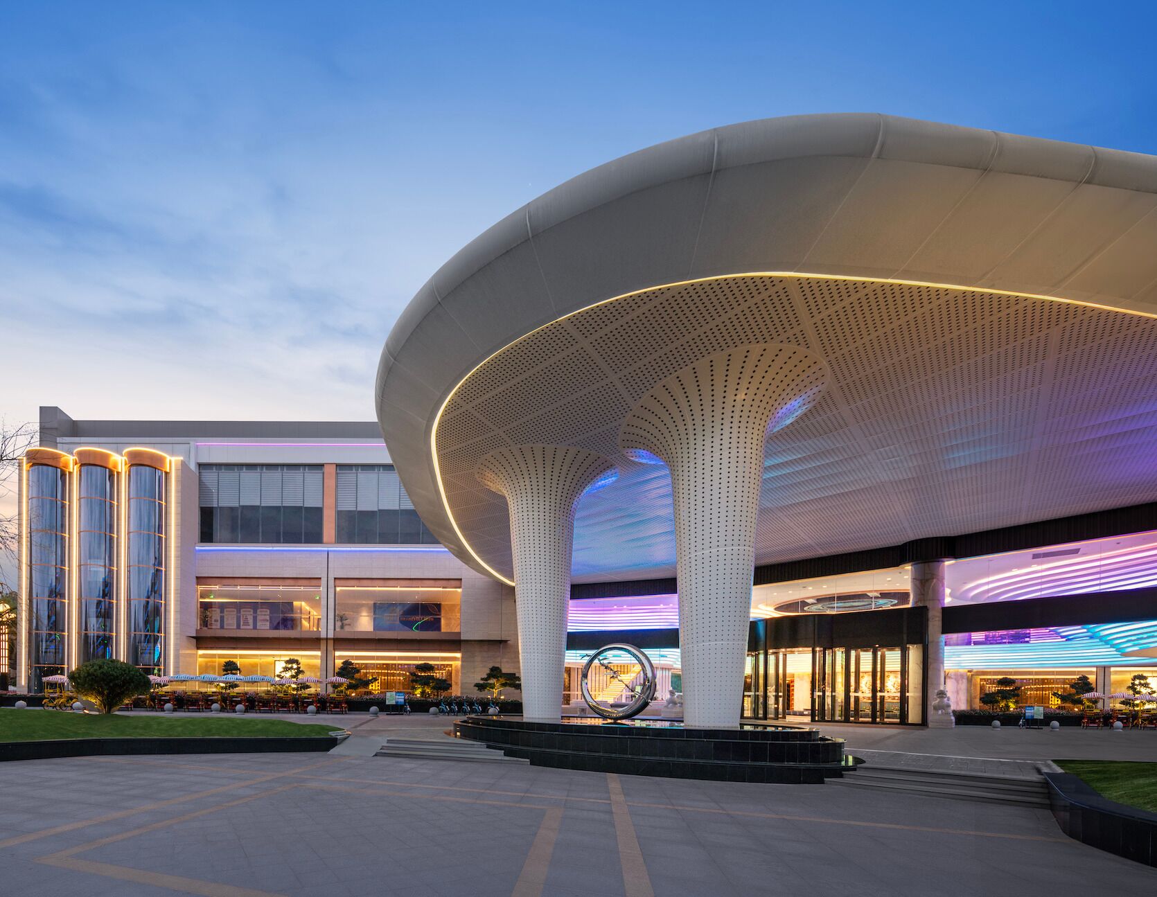 Un bâtiment moderne, avec une grande structure de toit ajouré, blanche, qui se trouve au premier plan.