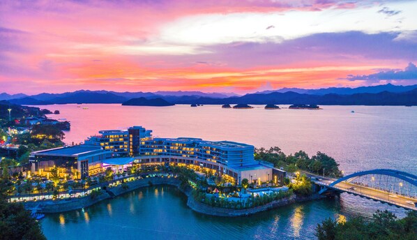 A waterfront hotel with a curved building, a bridge, and a view of the water and mountains. - MINHO INTENATIONAL RESORT (Hangzhou)