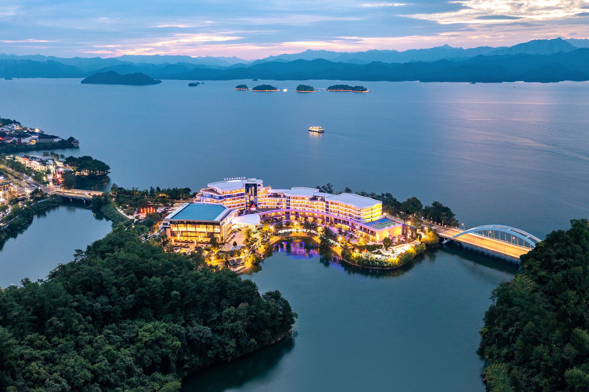 A waterfront hotel with multiple buildings, a bridge, and a large body of water with islands.