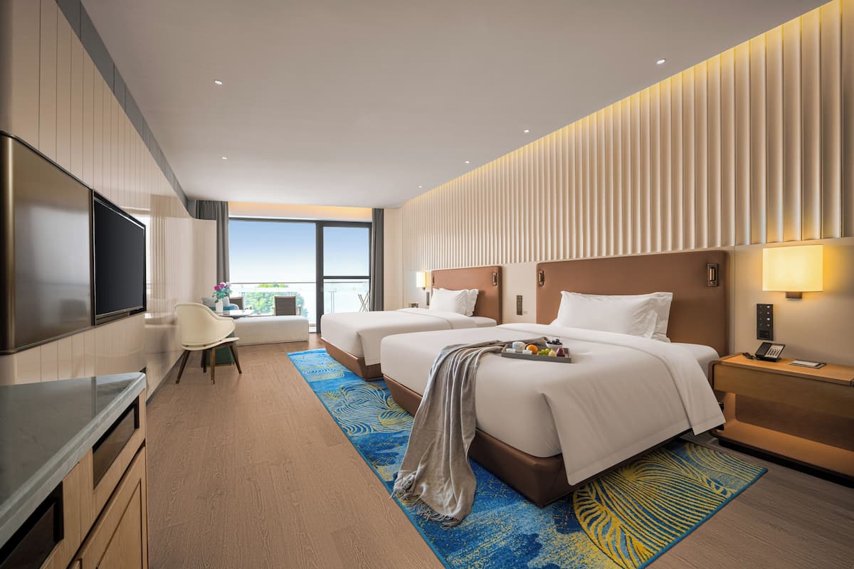 Une chambre d’hôtel moderne dotée de deux lits, d’une télévision à écran plat, d’un bureau et d’une grande fenêtre donnant sur la ville.