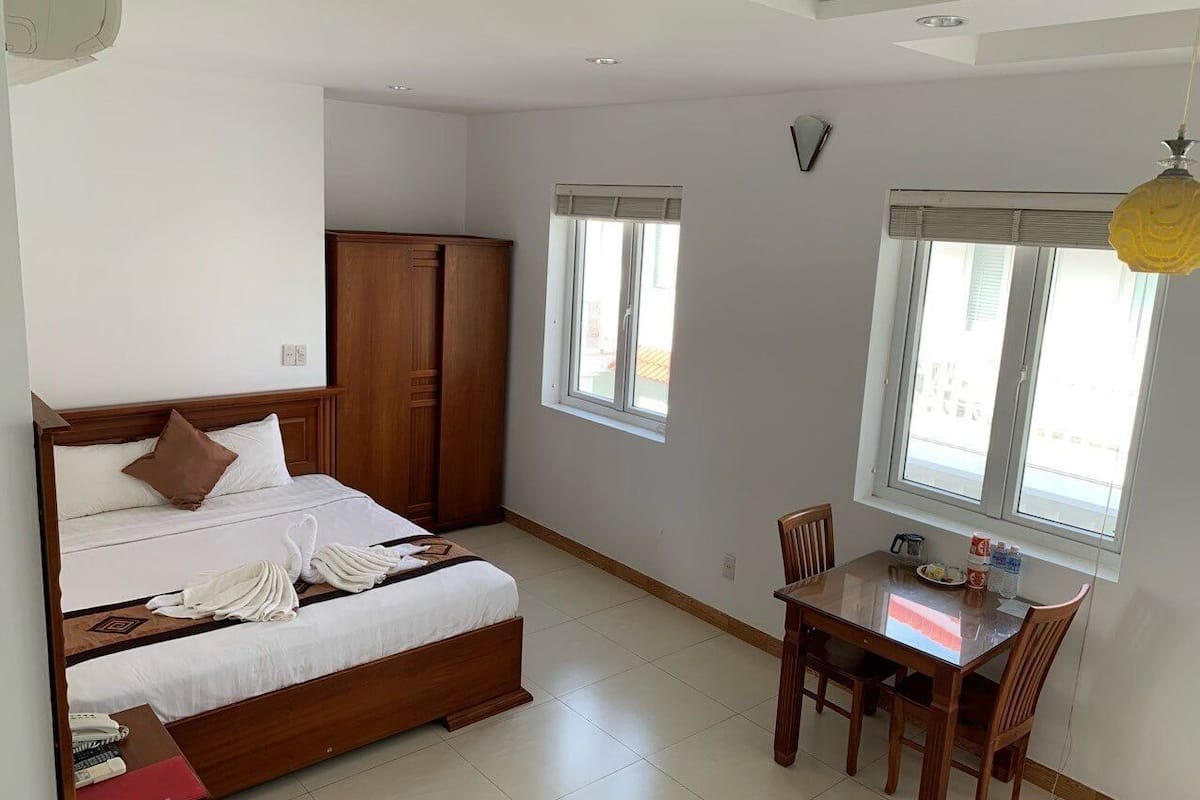A hotel room with a bed, a desk, and a chair. There is a window with blinds and a door with a mirror above it.