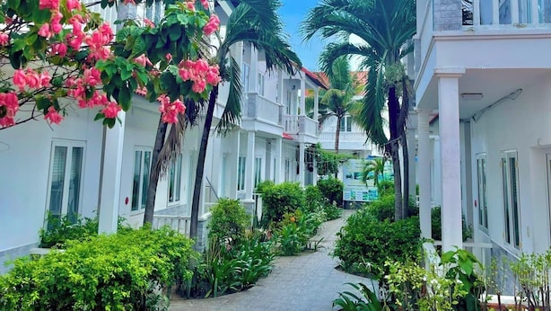 A pathway leading to a white building with balconies, surrounded by lush greenery and flowering plants. - Volga Hotel & Appartment Mui Ne (Mui Ne)