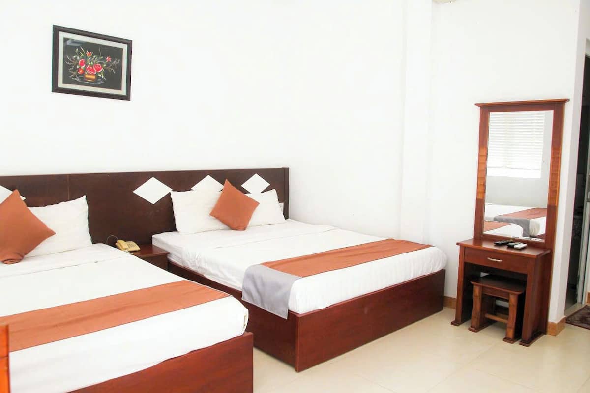 A hotel room with two beds, a wooden headboard, a bedside table with a lamp, a mirror, and a framed picture on the wall.