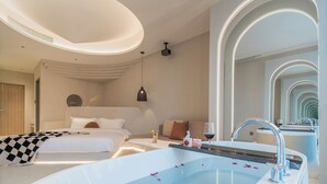 A modern hotel room with a large bed, a separate sofa, a bathtub with rose petals, and a large mirror reflecting the room. - Ziggy Hotel (Changsha)