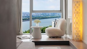 A modern room with a large window, a white chair, a small table with a vase, and a floor lamp. - Ziggy Hotel (Changsha)