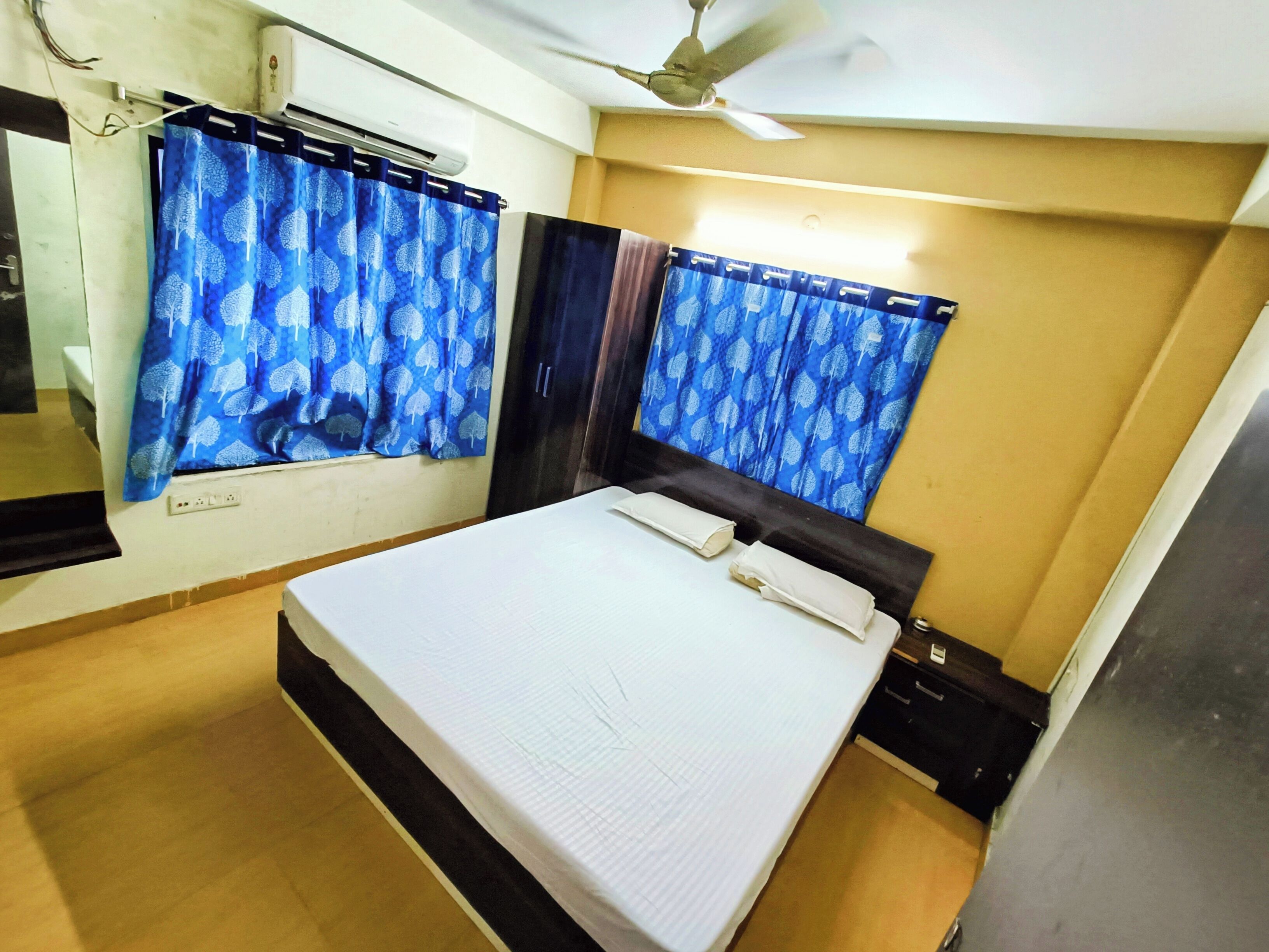 Une chambre à coucher avec un lit, un ventilateur de plafond et une fenêtre avec des rideaux bleus.