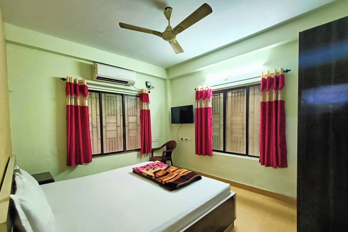 A bedroom with a bed, a ceiling fan, an air conditioning unit, and two windows with curtains.