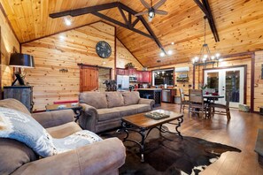 L’intérieur d’une cabane en rondins, avec un canapé, une table basse, une table à manger et un coin cuisine.