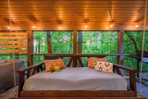 Un lit en bois donnant sur une forêt, un luminaire suspendu et une petite table avec une boîte et une télécommande.