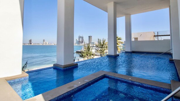 A rooftop infinity pool with a view of the city skyline and the sea.
