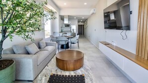 A modern living room with a grey sofa, a wooden coffee table, and a dining area with a table and chairs.