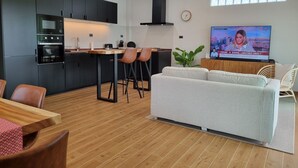 Ett modernt kök med mörka skåp, ett matbord i trä och en tv-skärm som visar ett nyhetsprogram.