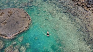 A person swimming in a clear, rocky pool surrounded by large rocks.