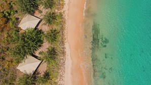 An aerial view of a beach with three white tents and dense green foliage.