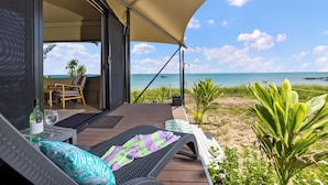 A beachside patio with a view of the ocean, a covered seating area, and a table with a bottle and glass.