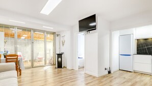 Un amplio salón con piso de madera, un televisor de pantalla plana montado en la pared y una puerta corrediza de vidrio que da a un patio exterior.