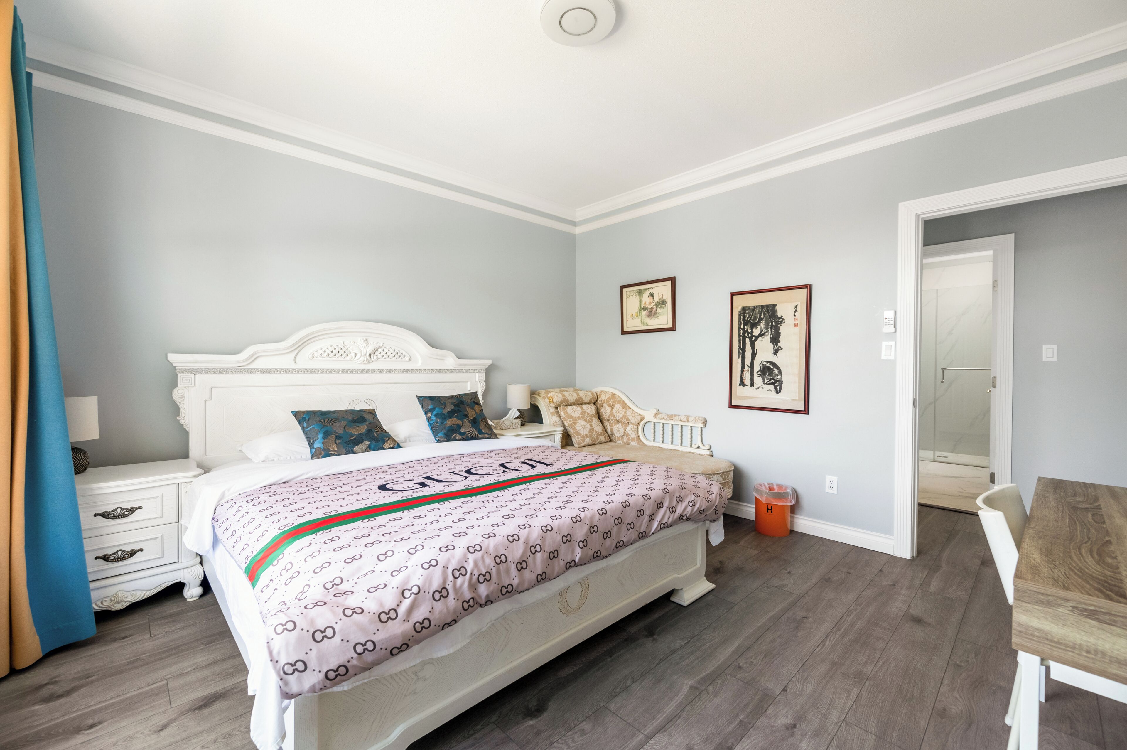 Une chambre à coucher comprenant un lit, des tables de chevet, une table en bois et une porte donnant sur une salle de bain.