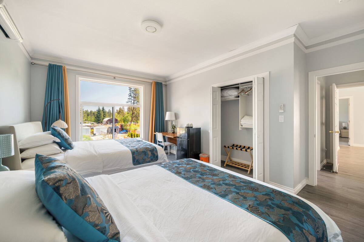 A hotel room with two beds, a desk, a TV, and a closet.