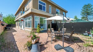 A two-story house with a patio area featuring a table and chairs, a covered seating area, and a fenced garden. - Amy Guesthouse (Richmond)