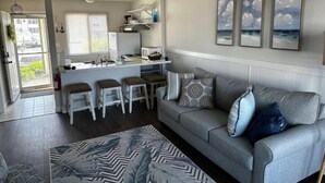 Una sala de estar moderna con un sofá gris, un tapete estampado y una zona de cocina con un taburete de bar.