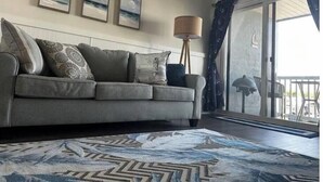 Una sala de estar con un sofá gris, cojines estampados, una lámpara de pie y vistas al balcón.