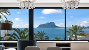A modern room with a large window offering a view of the sea and a mountain. There are two chairs and a table in the room.