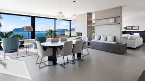 A modern living room with a dining area, large windows with a view of the sea, and a built-in seating area.