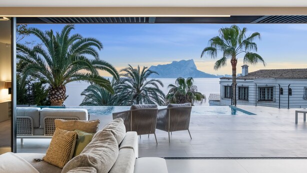 A modern living room with a sofa, chairs, and a view of a pool and mountains.