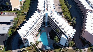 An aerial view of a hotel with a central courtyard, multiple floors, and a pool. - Just Beachy (Corpus Christi)