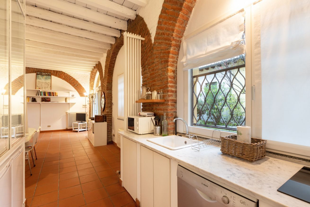 A kitchen with white cabinets, a Bosch dishwasher, a window with a view, and a brick wall.