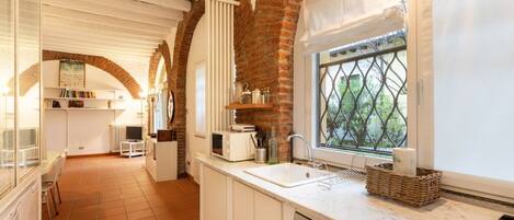 A kitchen with white cabinets, a Bosch dishwasher, a window with a view, and a brick wall.