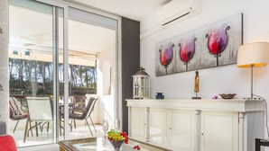 A modern living room with a glass coffee table, a white cabinet, and a painting of wine glasses.