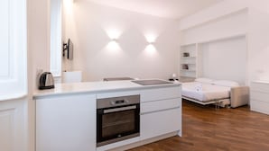 Un dormitorio moderno y funcional con cama integrada, una kitchenette pequeña y un armario blanco.