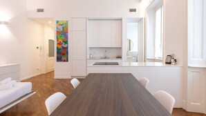 Una cocina moderna con armarios blancos, una isla central con pileta y una zona de comedor con una mesa larga y sillas.