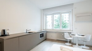 Eine moderne Küche mit großem Fenster, Backofen und einer kleinen Essecke mit zwei weißen Stühlen und einem Tisch.