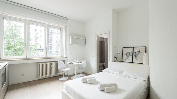 Ein modernes Hotelzimmer mit einem großen Bett, einem Schreibtisch, einem Stuhl und einem Fenster mit Blick auf Gebäude und Bäume.