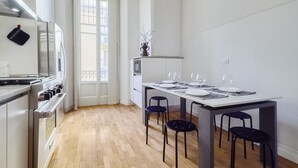 Una cocina moderna con comedor, que cuenta con una encimera blanca, electrodomésticos de acero inoxidable y piso de madera.
