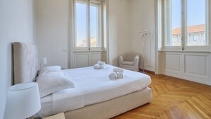 Una habitación de hotel con una cama grande, dos ventanas, una silla y una lámpara.