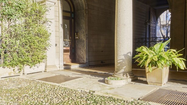 Un edificio de piedra con arcos y columnas, una planta en maceta y un camino de grava.