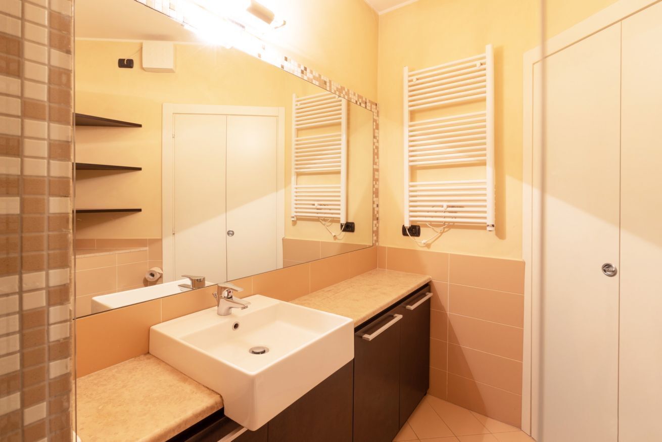 A bathroom with a white sink, dark cabinets, a mirror, and towel racks.