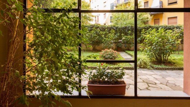 A window with a view of a courtyard, a potted plant, and a building in the background. - Ampio Trilocale in zona Solari - Mirable PM (Milano)